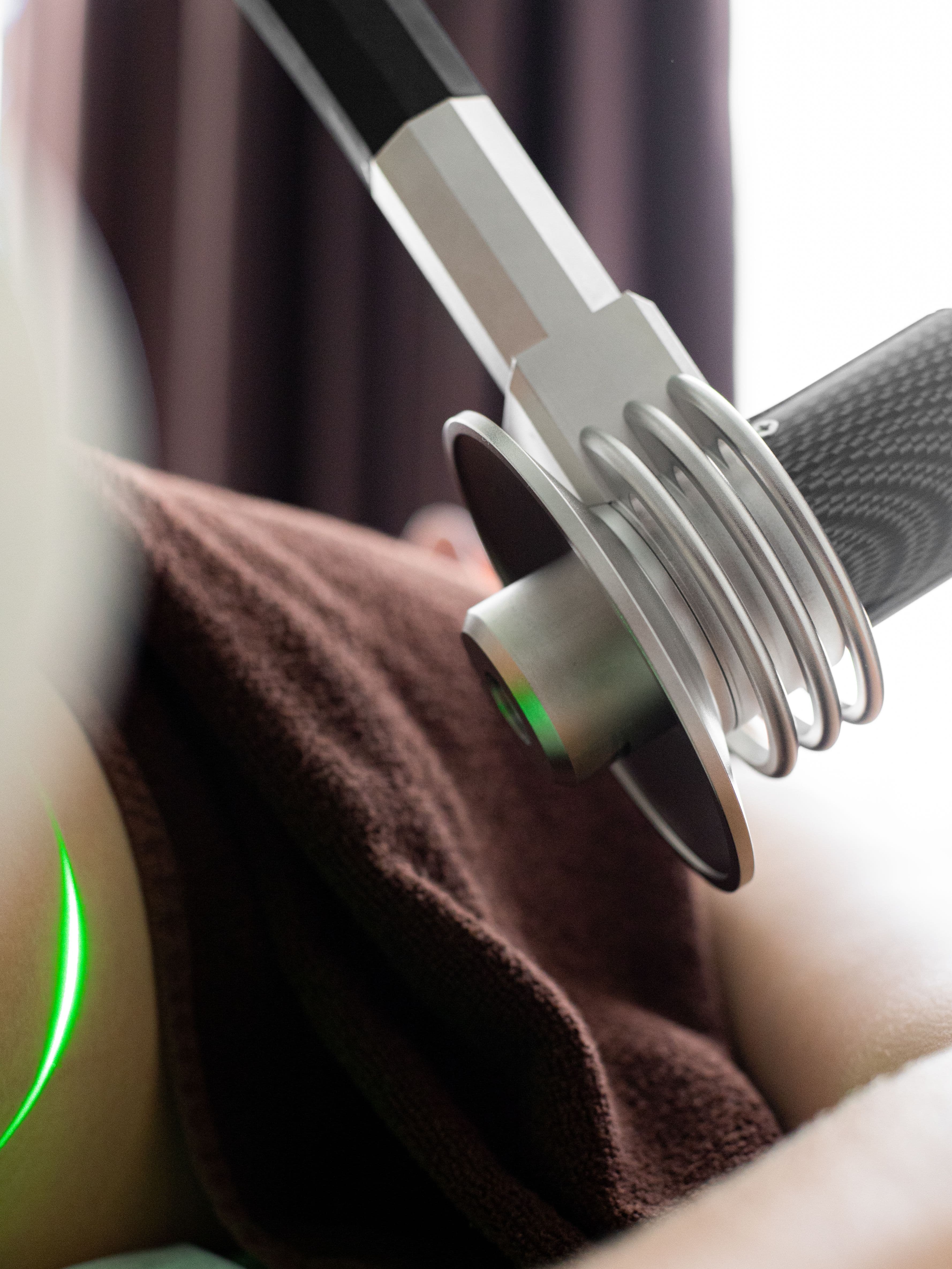 Close-up of a medical laser device emitting green light onto a person's skin during treatment.